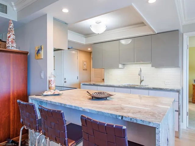 Kitchen with a breakfast bar area, light stone countertops, a peninsula, ornamental molding, and backsplash