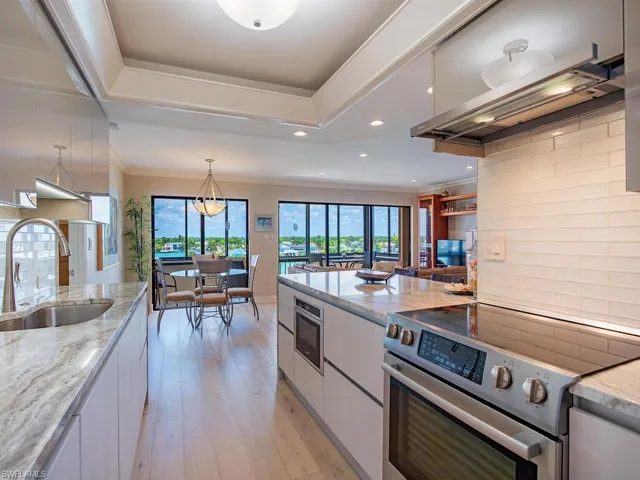 Kitchen featuring stainless steel appliances, light stone counters, light wood finished floors, exhaust hood, and hanging light fixtures