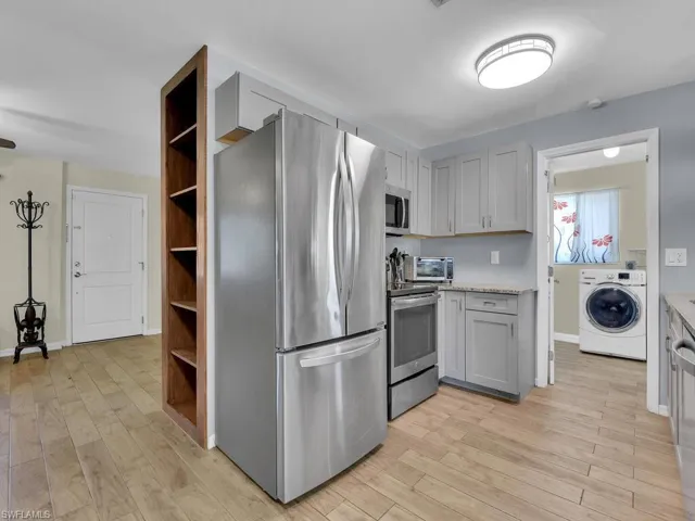 Kitchen featuring stainless steel appliances, light wood-type flooring, washer / dryer, light stone counters, and gray cabinetry