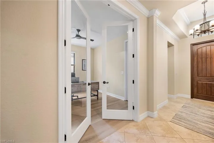 Entrance foyer featuring light tile patterned flooring, baseboards, crown molding, and ceiling fan with notable chandelier