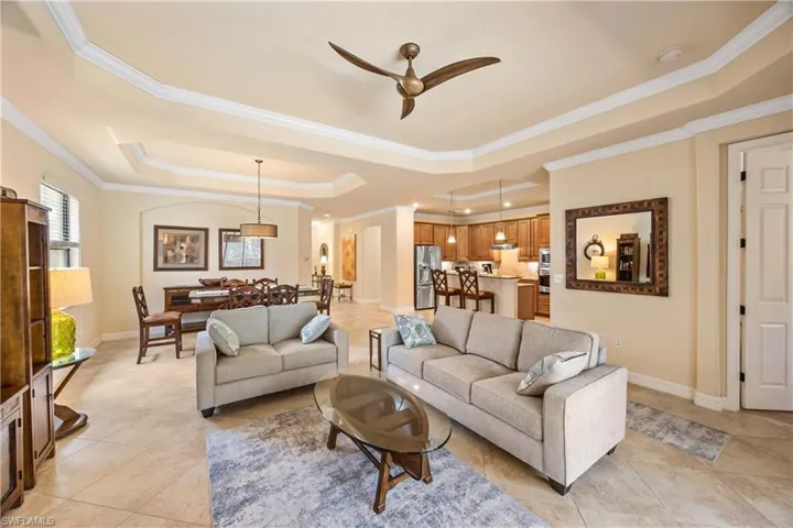 Living area featuring a ceiling fan, a raised ceiling, light tile patterned floors, and baseboards