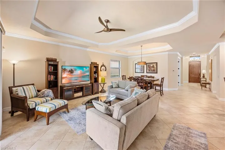 Living room featuring crown molding, baseboards, ceiling fan, a raised ceiling, and light tile patterned floors
