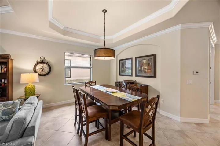 Dining space featuring baseboards, a tray ceiling, crown molding, and light tile patterned floors