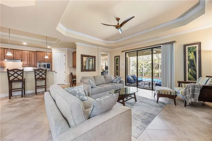 Living area featuring light tile patterned flooring, crown molding, a ceiling fan, a raised ceiling, and baseboards