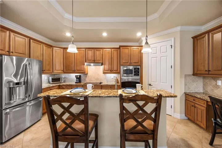 Kitchen with a tray ceiling, brown cabinets, light stone countertops, and stainless steel appliances
