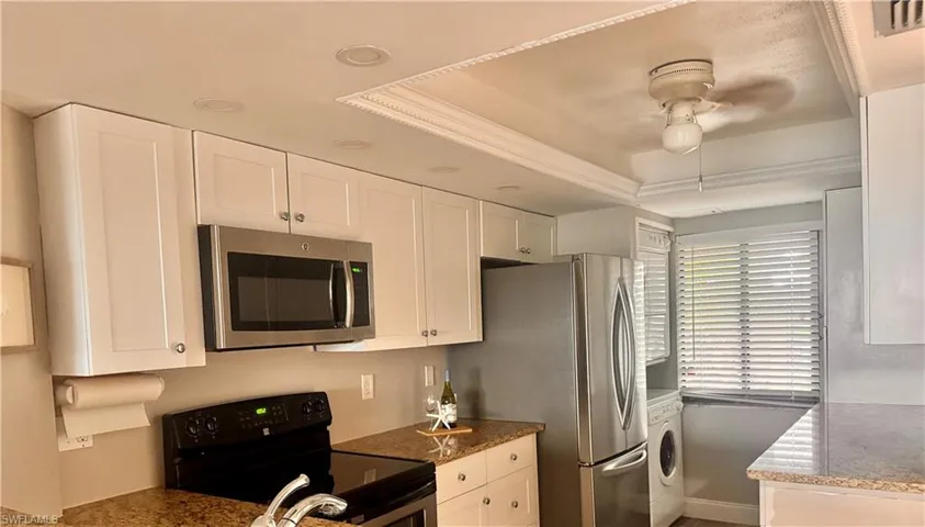 Kitchen with stainless steel appliances, a raised ceiling, white cabinets, and ornamental molding