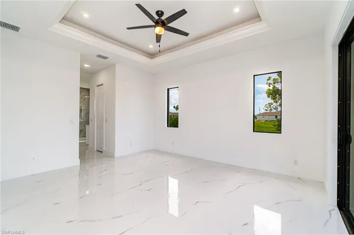 Primary bedroom with light tile patterned floors, a healthy amount of sunlight, ceiling fan, and tray ceiling