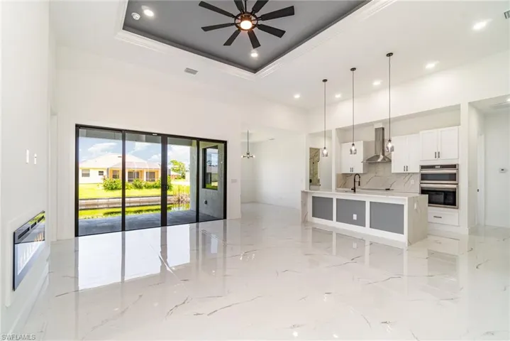 Kitchen with quartz backsplash, wall chimney exhaust hood, stainless steel double oven, raised ceiling, and light tile patterned floors
