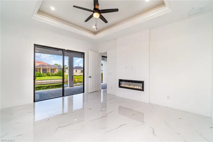 Primary bedroom with recessed wall mounted remote control fireplace, ceiling fan, and impact resistant sliding doors