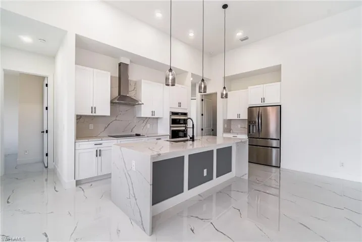 Kitchen with quartz backsplash, stainless steel appliances, wall chimney exhaust hood, and an island with sink