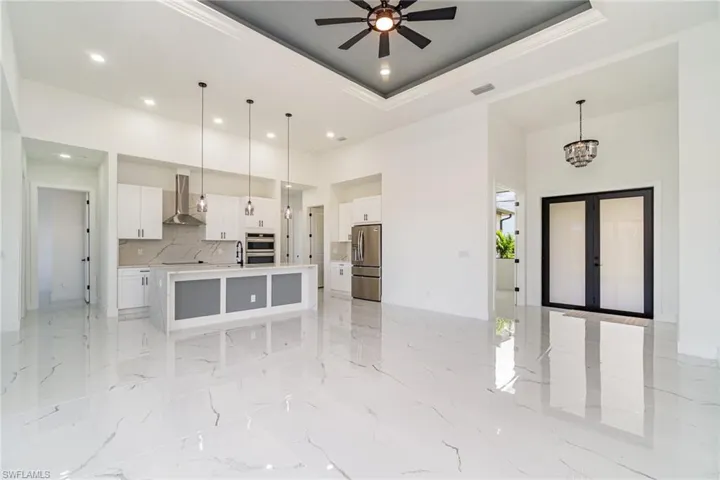 Kitchen with white 42" cabinets, ceiling fan, entryway chandelier, Frigidaire Gallery stainless steel appliances, wall chimney exhaust hood, and waterfall quartz center island with sink