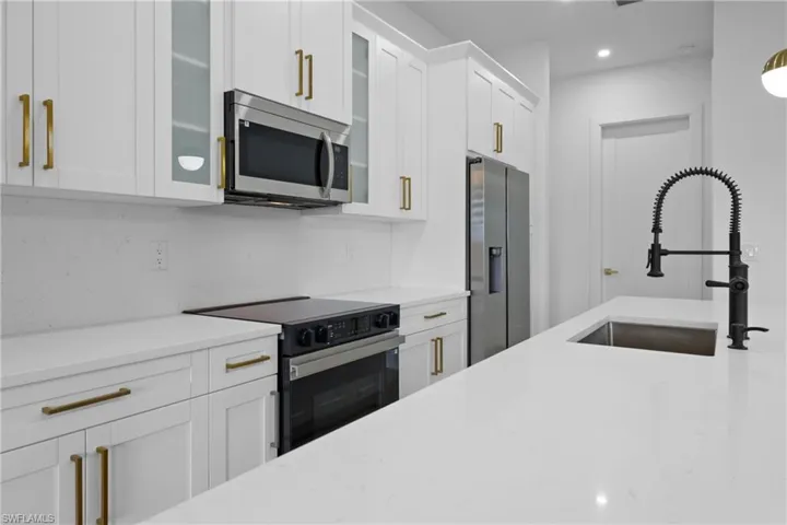 Kitchen with appliances with stainless steel finishes, a sink, white cabinets, glass insert cabinets, and light stone counters