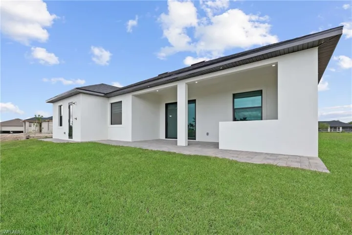 Back of house with stucco siding, a yard, and a patio