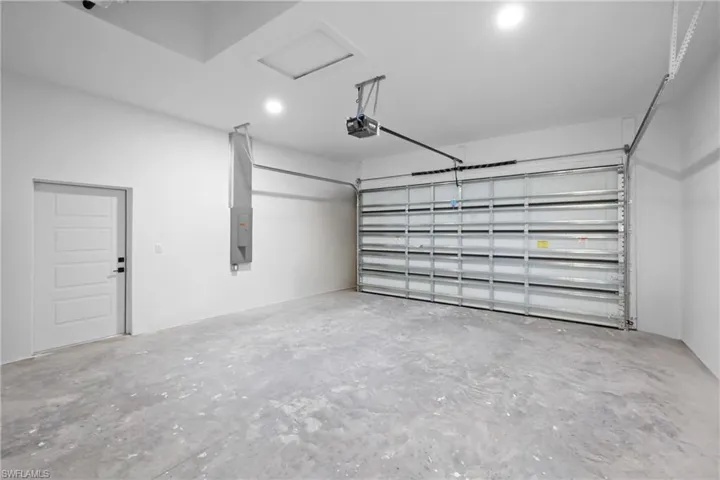 Garage with electric panel, a garage door opener, and recessed lighting
