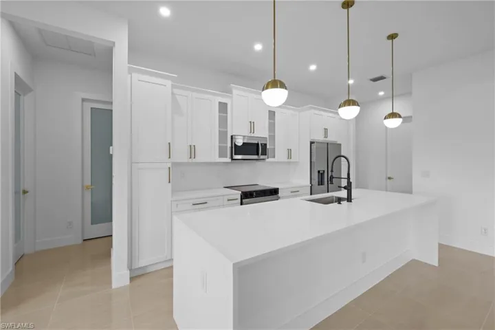 Kitchen with stainless steel appliances, a sink, a kitchen island with sink, white cabinets, and light countertops