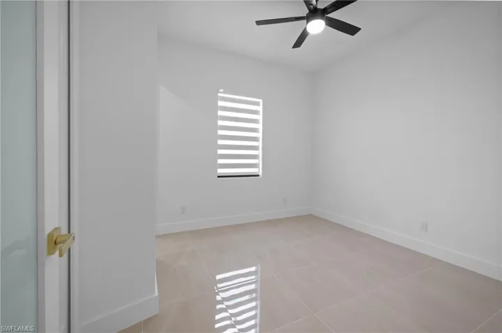 Empty room with a ceiling fan, baseboards, and light tile patterned floors