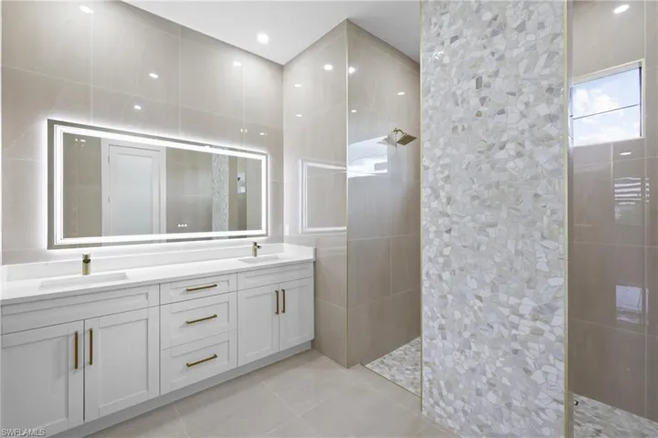 Bathroom with tile walls, a walk in shower, double vanity, and tile patterned flooring
