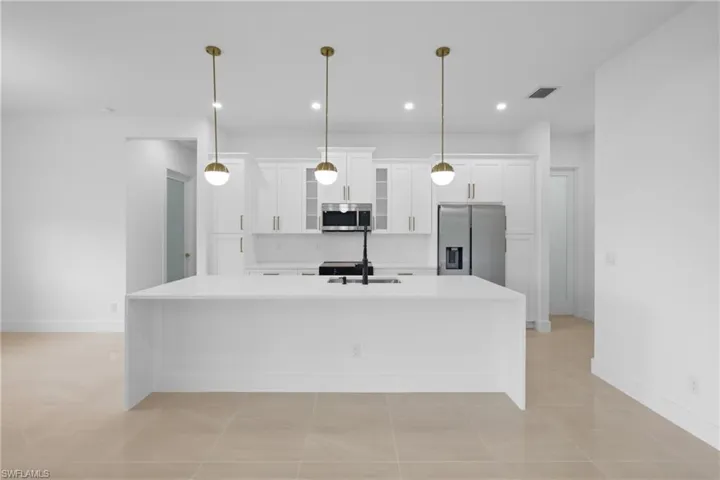 Kitchen featuring stainless steel appliances, white cabinets, light countertops, a kitchen island with sink, and baseboards