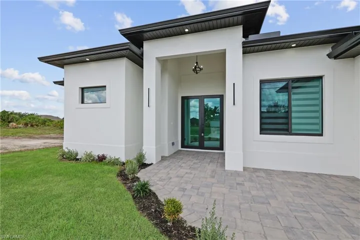 Doorway to property featuring stucco siding, a lawn, a patio area, and french doors