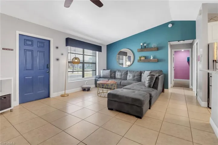 Living area featuring light tile patterned floors, ceiling fan, lofted ceiling, and baseboards