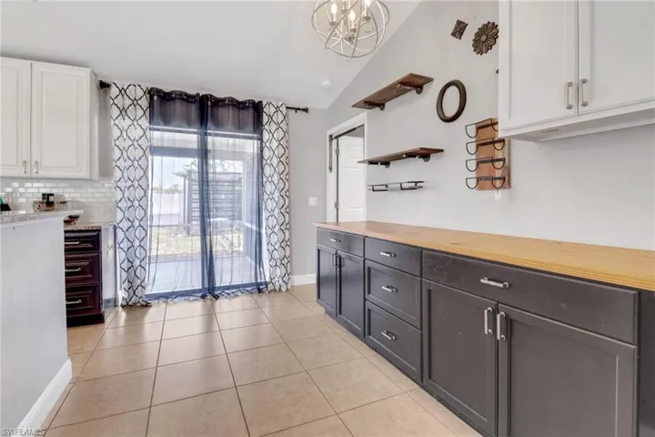 Kitchen with light tile patterned floors, butcher block counters, hanging light fixtures, white cabinetry, and backsplash