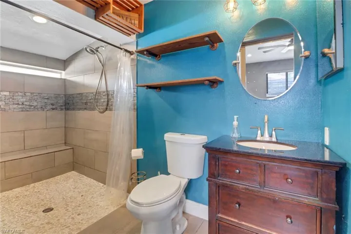 Bathroom with toilet, baseboards, tiled shower, and vanity