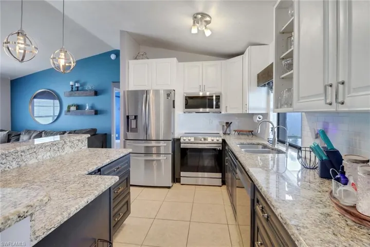 Kitchen with lofted ceiling, decorative light fixtures, stainless steel appliances, white cabinetry, and a sink