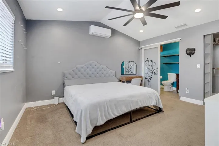 Bedroom featuring a wall unit AC, light carpet, visible vents, baseboards, and vaulted ceiling