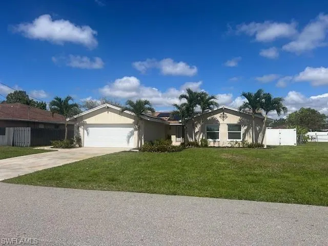 Ranch-style house with concrete driveway, a front lawn, an attached garage, and fence