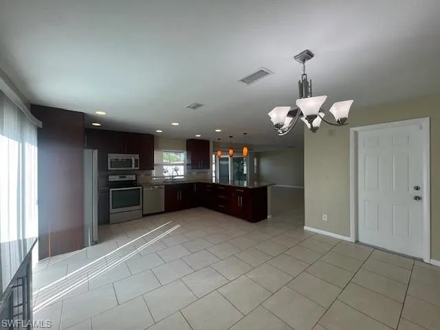 Kitchen with decorative light fixtures, light tile patterned floors, stainless steel appliances, visible vents, and open floor plan