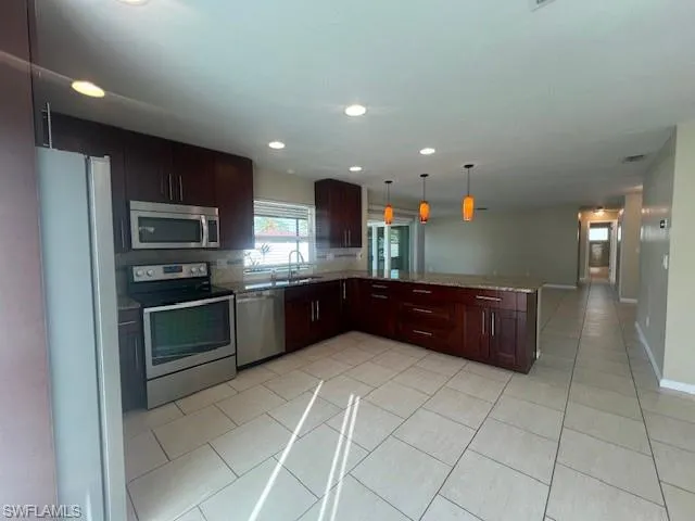 Kitchen with pendant lighting, appliances with stainless steel finishes, open floor plan, a sink, and a peninsula