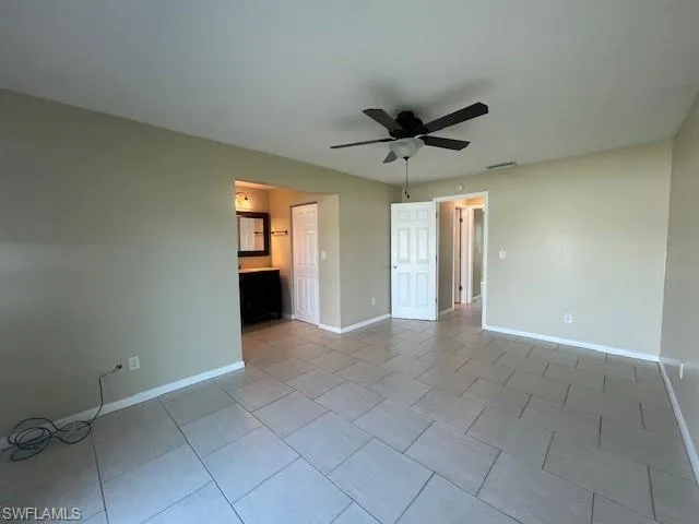 Empty room with light tile patterned flooring, ceiling fan, visible vents, and baseboards