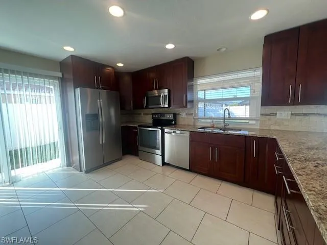 Kitchen featuring appliances with stainless steel finishes, a sink, backsplash, and light stone countertops