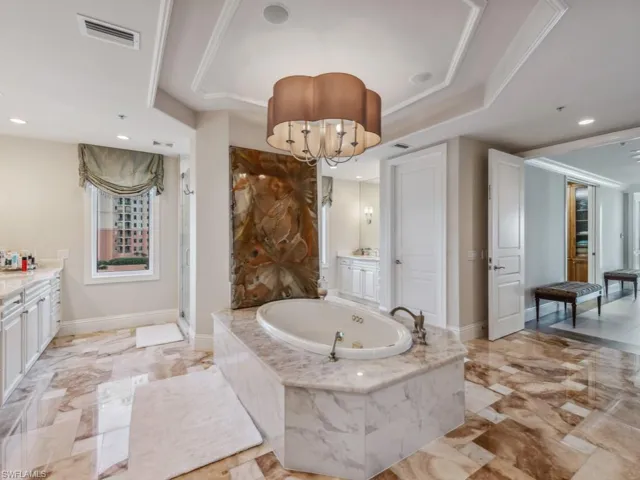 Bathroom with ornamental molding, vanity, a raised ceiling, tiled tub, and a chandelier
