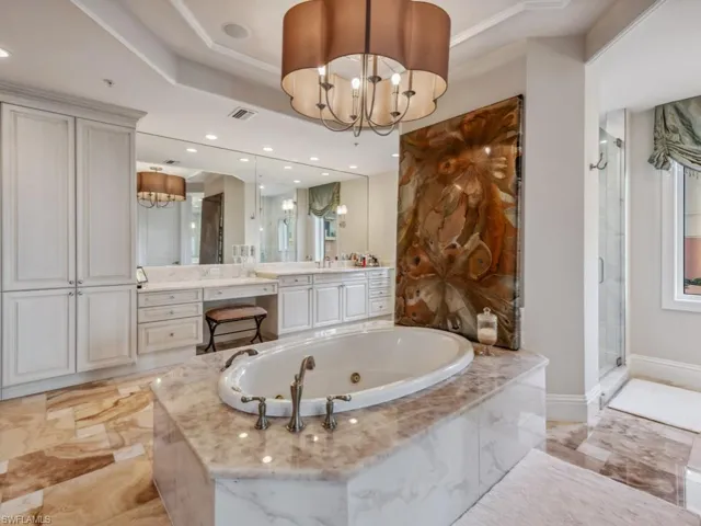 Bathroom featuring vanity, plus walk in shower, a raised ceiling, ornamental molding, and a notable chandelier