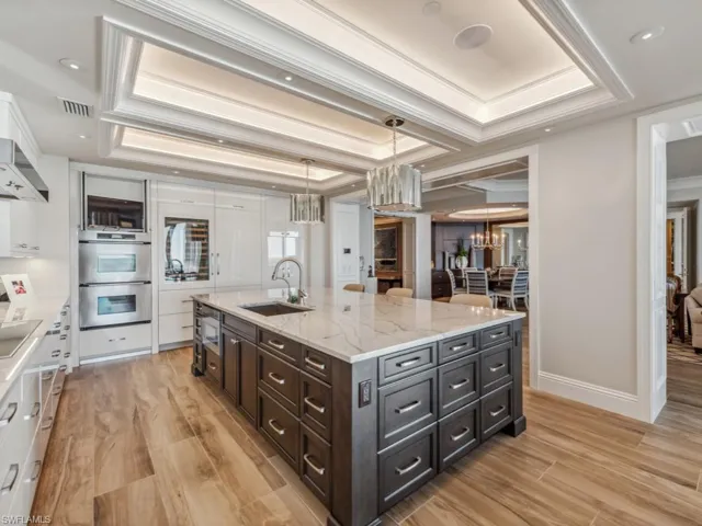 Kitchen with pendant lighting, a tray ceiling, white cabinetry, and sink