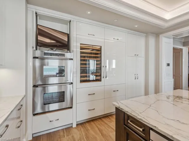 Kitchen with white cabinets, light stone countertops, crown molding, and double oven