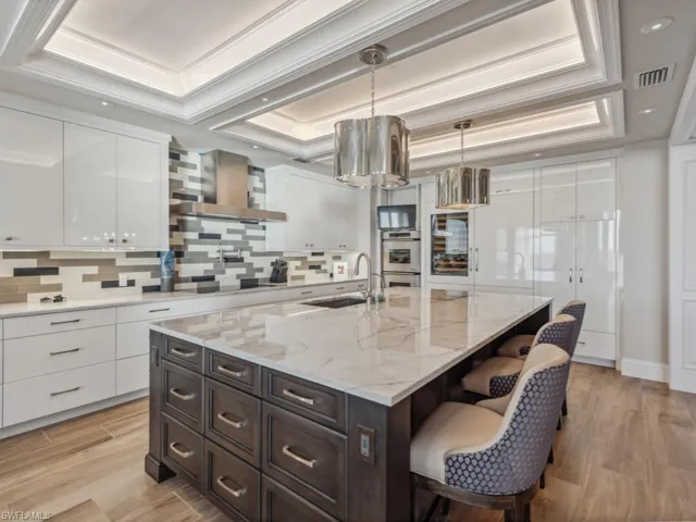 Kitchen with white cabinetry, sink, wall chimney exhaust hood, a raised ceiling, and a kitchen island with sink