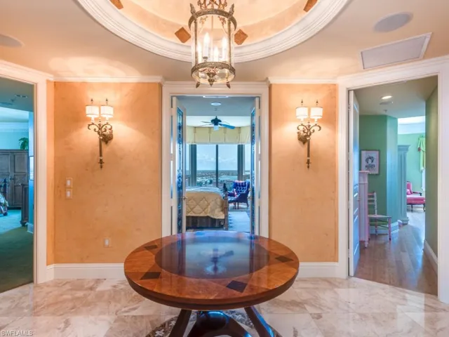 Corridor with a notable chandelier, a raised ceiling, and crown molding