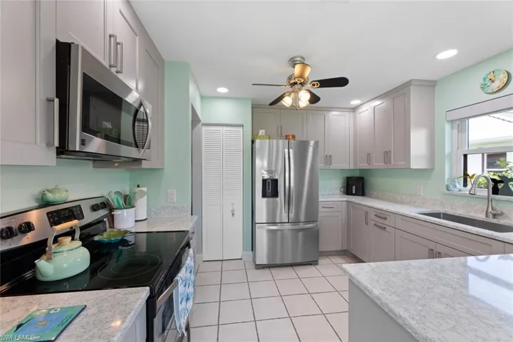Kitchen featuring appliances with stainless steel finishes, light stone counters, sink, light tile flooring, and ceiling fan