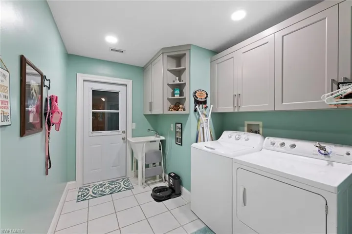 Spacious laundry room includes  washer and dryer, laundry tub, light tile flooring & new cabinetry for additional storage