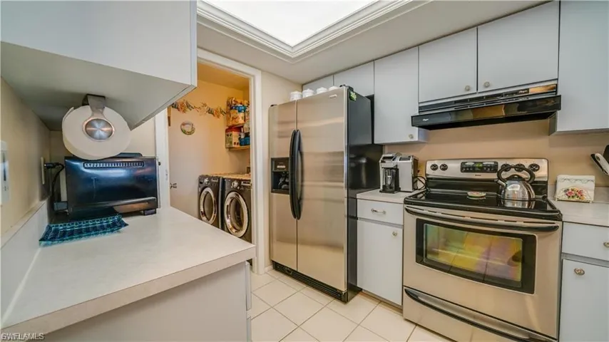 Kitchen featuring stainless steel appliances, washer and dryer, light countertops, ventilation hood, and gray cabinets