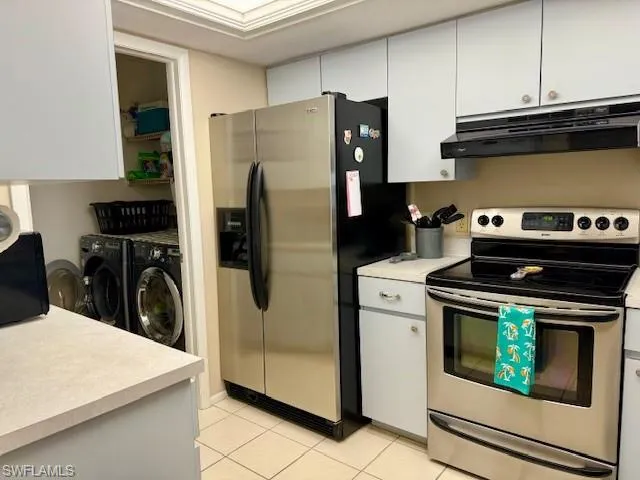 Kitchen with stainless steel appliances, light countertops, white cabinets, washing machine and clothes dryer, and light tile patterned floors