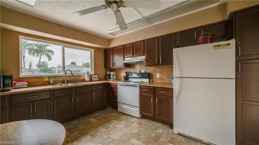 Kitchen with white appliances, dark wood finish cabinets, a ceiling fan, light countertops, and stone finish floors