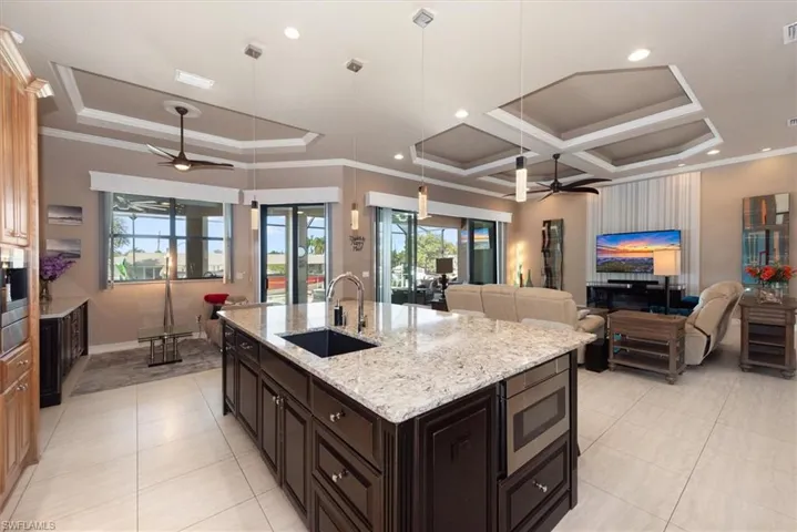 Kitchen with ceiling fan, light stone counters, a large island, open floor plan, and crown molding