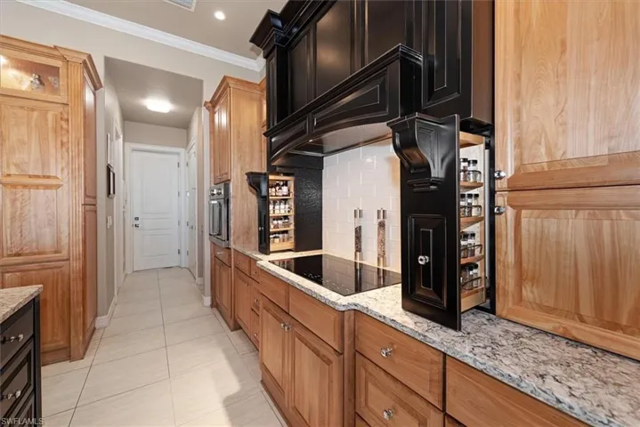 Kitchen featuring light stone counters, crown molding, light tile patterned floors, black electric cooktop, and stainless steel oven
