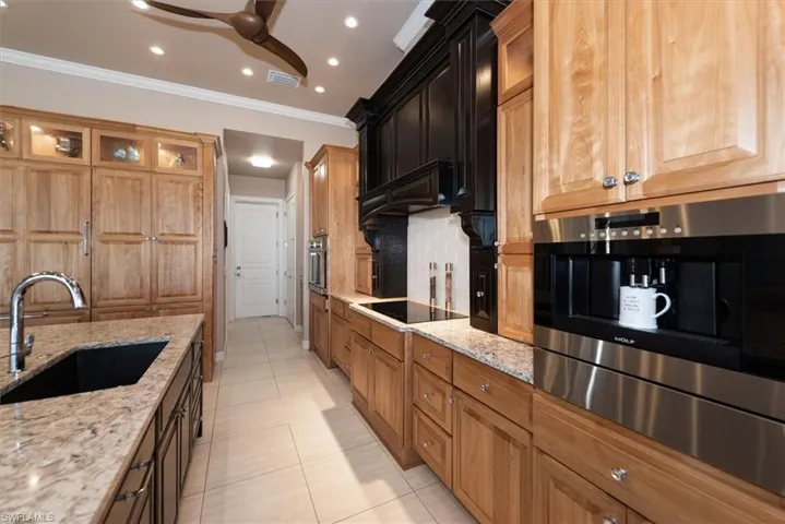 Kitchen featuring light stone counters, glass insert cabinets, a ceiling fan, crown molding, and light tile patterned floors