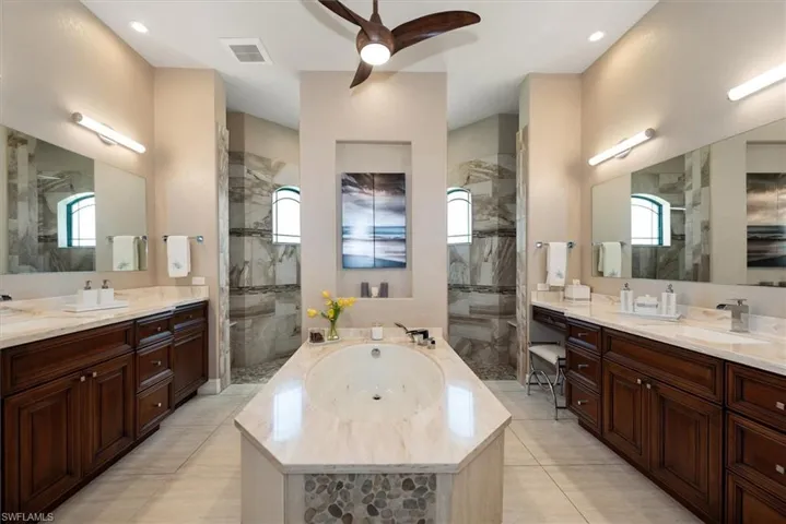 Bathroom with a jetted tub, ceiling fan, a marble finish shower, two vanities, and recessed lighting
