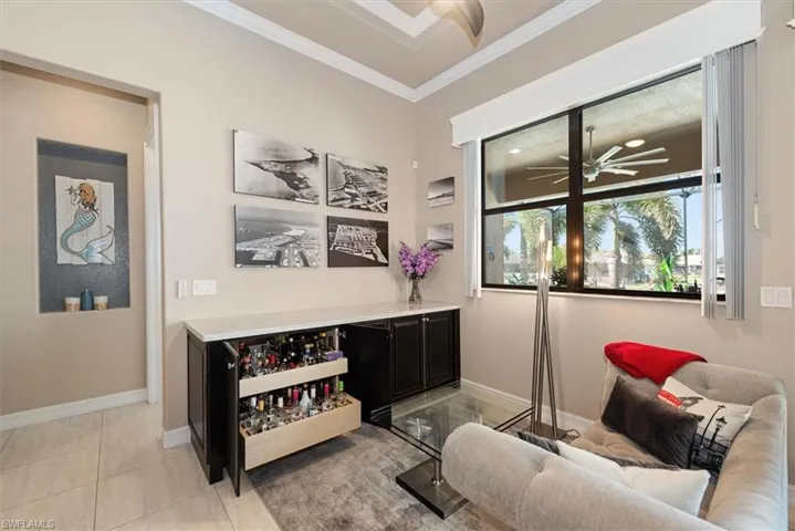 Bar area featuring dark cabinets, a ceiling fan, ornamental molding, light stone countertops, and light tile patterned flooring