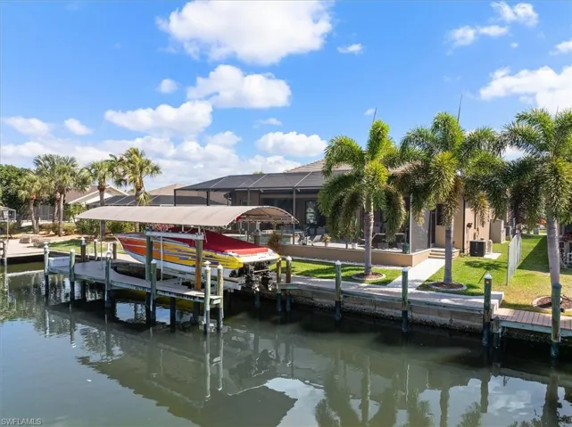 Dock area with boat lift, a water view, a sunroom, a lawn, and a lanai